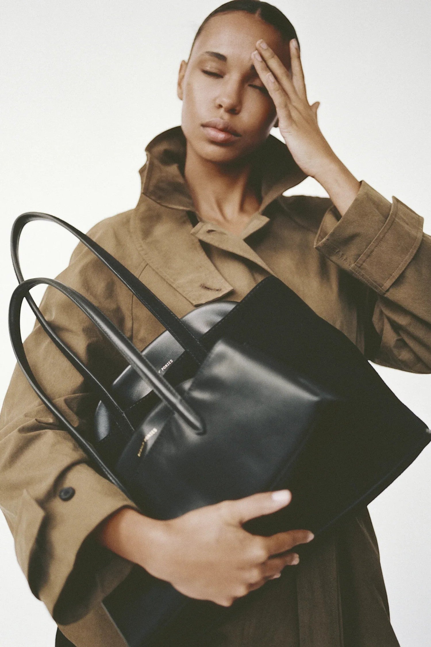 Model holding an ELSHAM BOUTIQUE black calf nappa leather slouchy bag with brass hardware and gold logo detail.