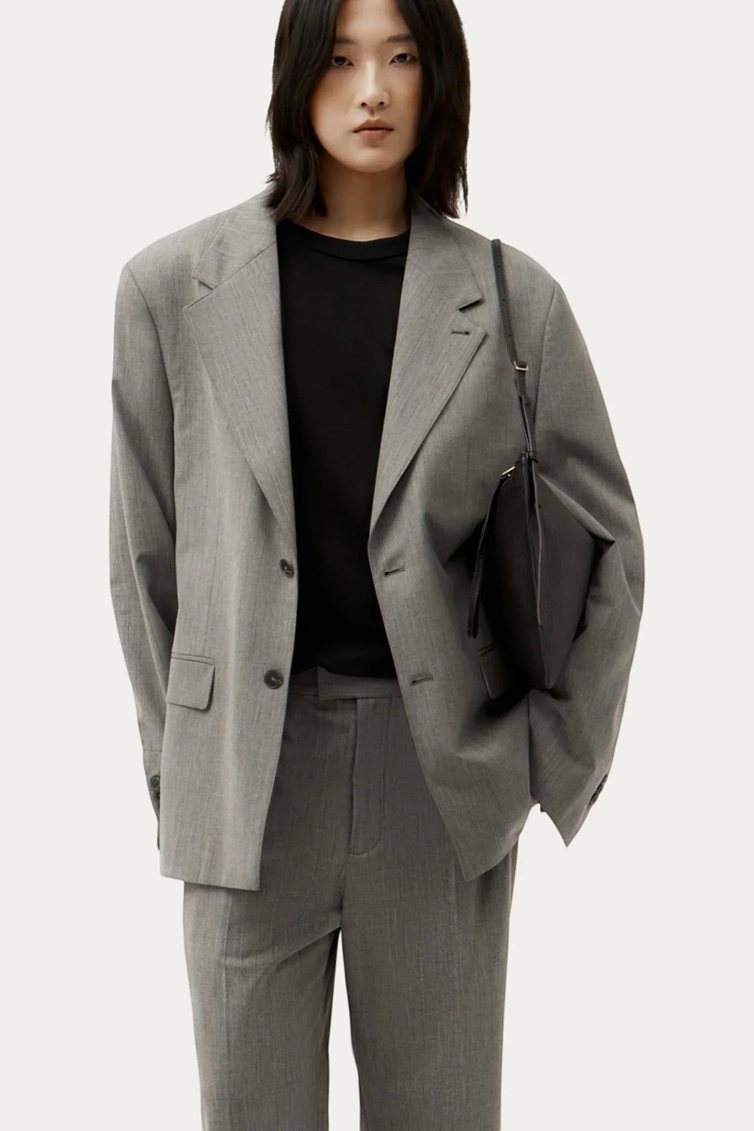 ELSHAM BOUTIQUE Mini Chopalopagus black leather crossbody bag with brass hardware worn by a model in a grey suit.