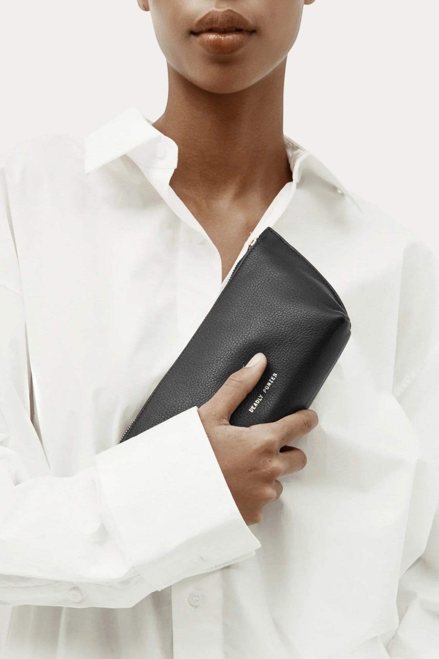 ELSHAM BOUTIQUE medium black calf nappa leather pouch with brass hardware held by a model in a white shirt