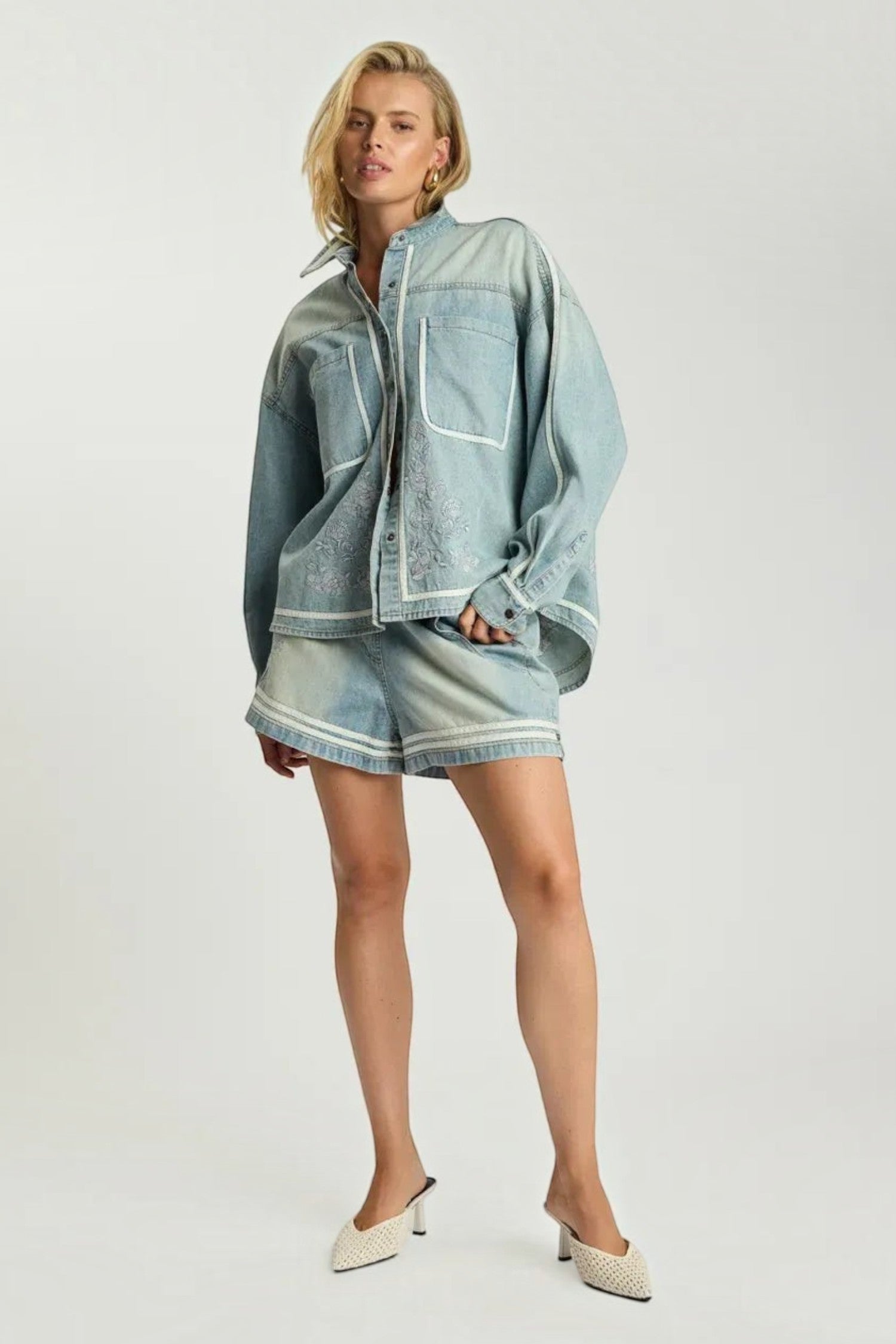 Model wearing ELSHAM BOUTIQUE chambray blue denim shirt with artisan embroidery and matching shorts in a studio setting.