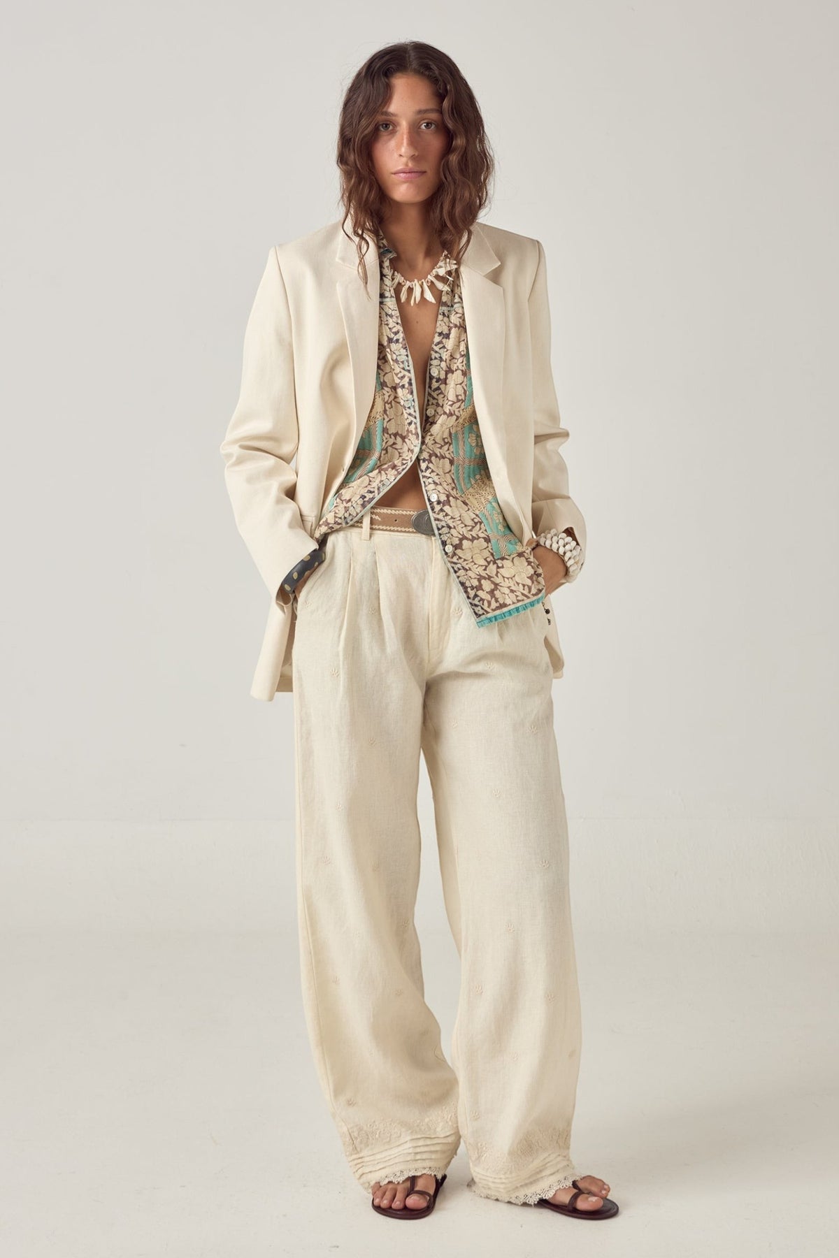 Model wearing ELSHAM BOUTIQUE Otto ivory cotton-linen straight-leg pants with subtle pleats and embroidered hem detail.
