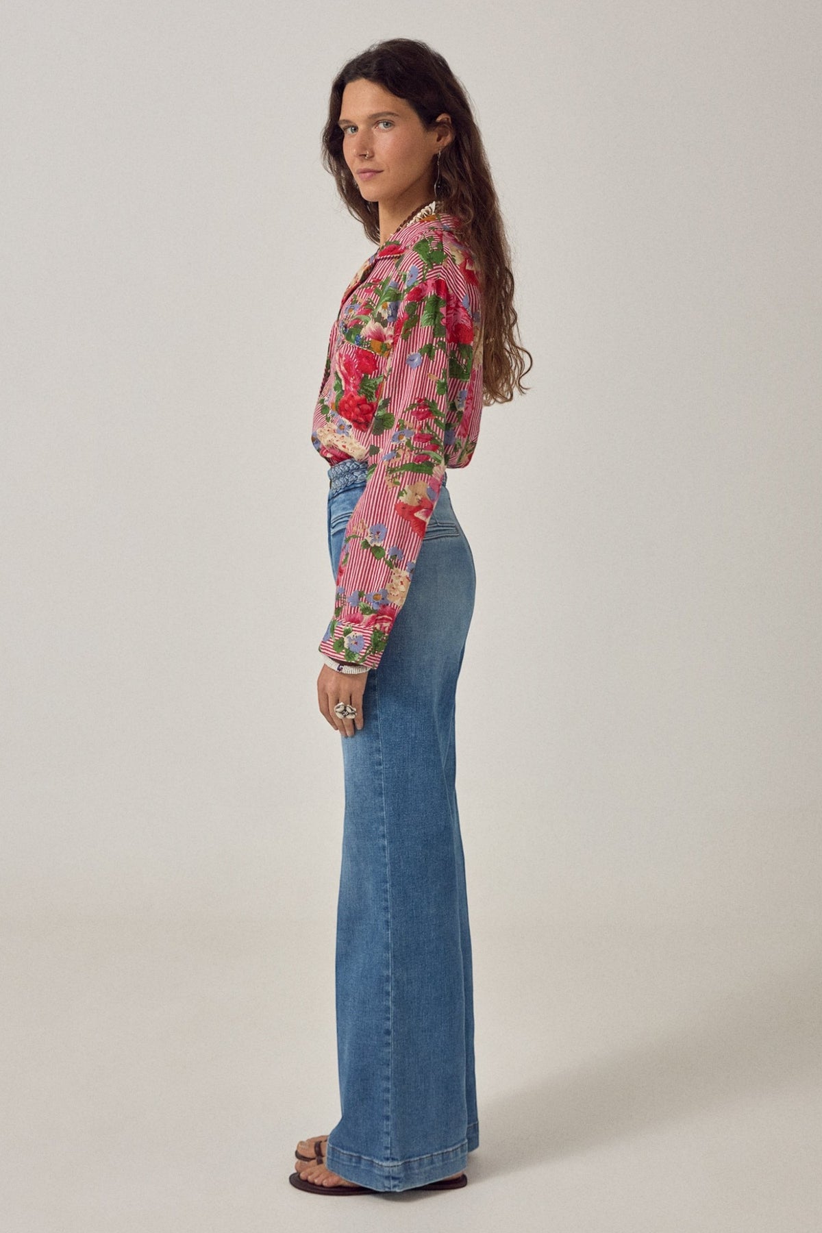 Model wearing ELSHAM BOUTIQUE Piti shirt in rouge with floral print and stripes, paired with blue flared jeans.
