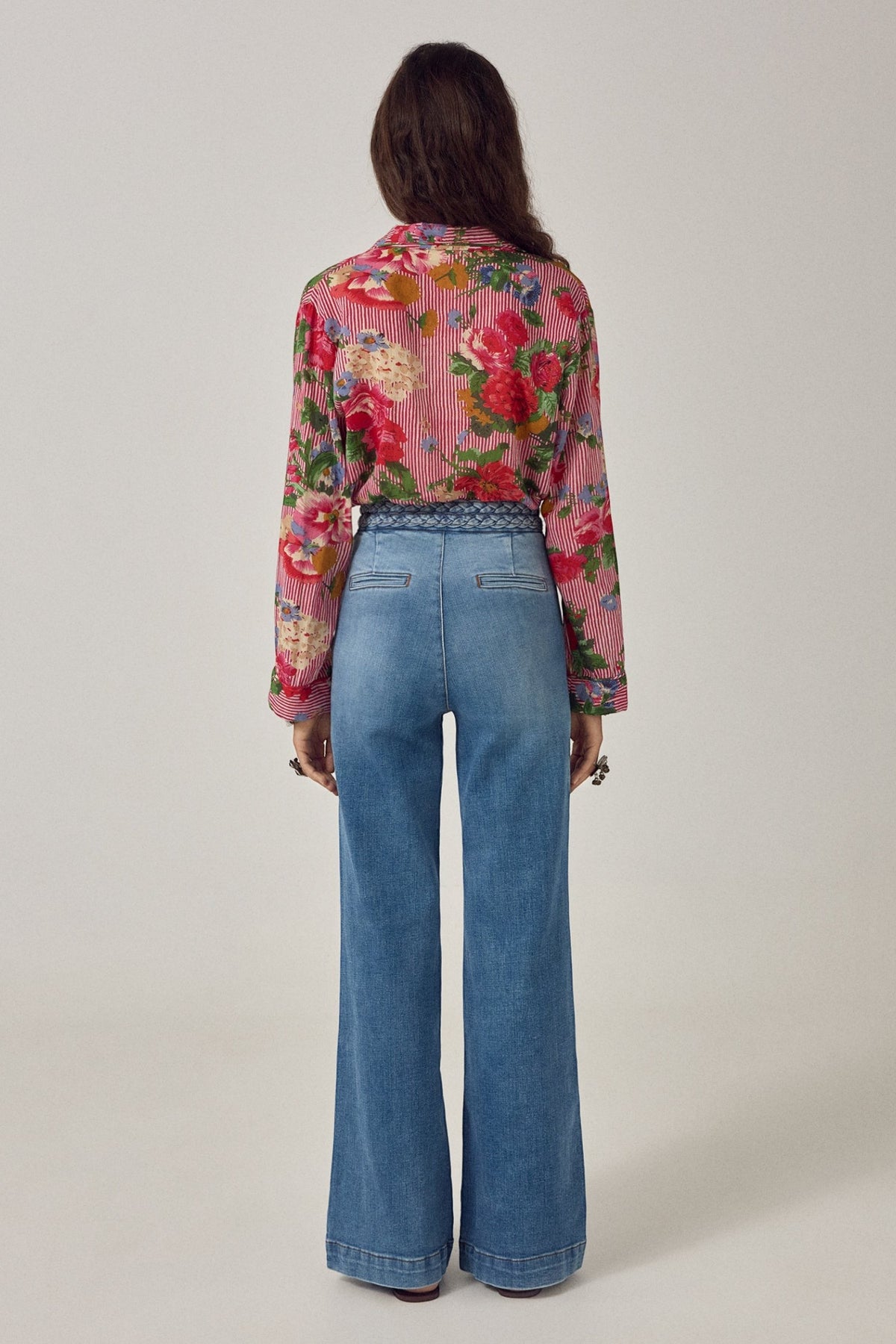 Back view of ELSHAM BOUTIQUE Piti shirt in rouge floral print over stripes, worn tucked into blue wide-leg jeans.