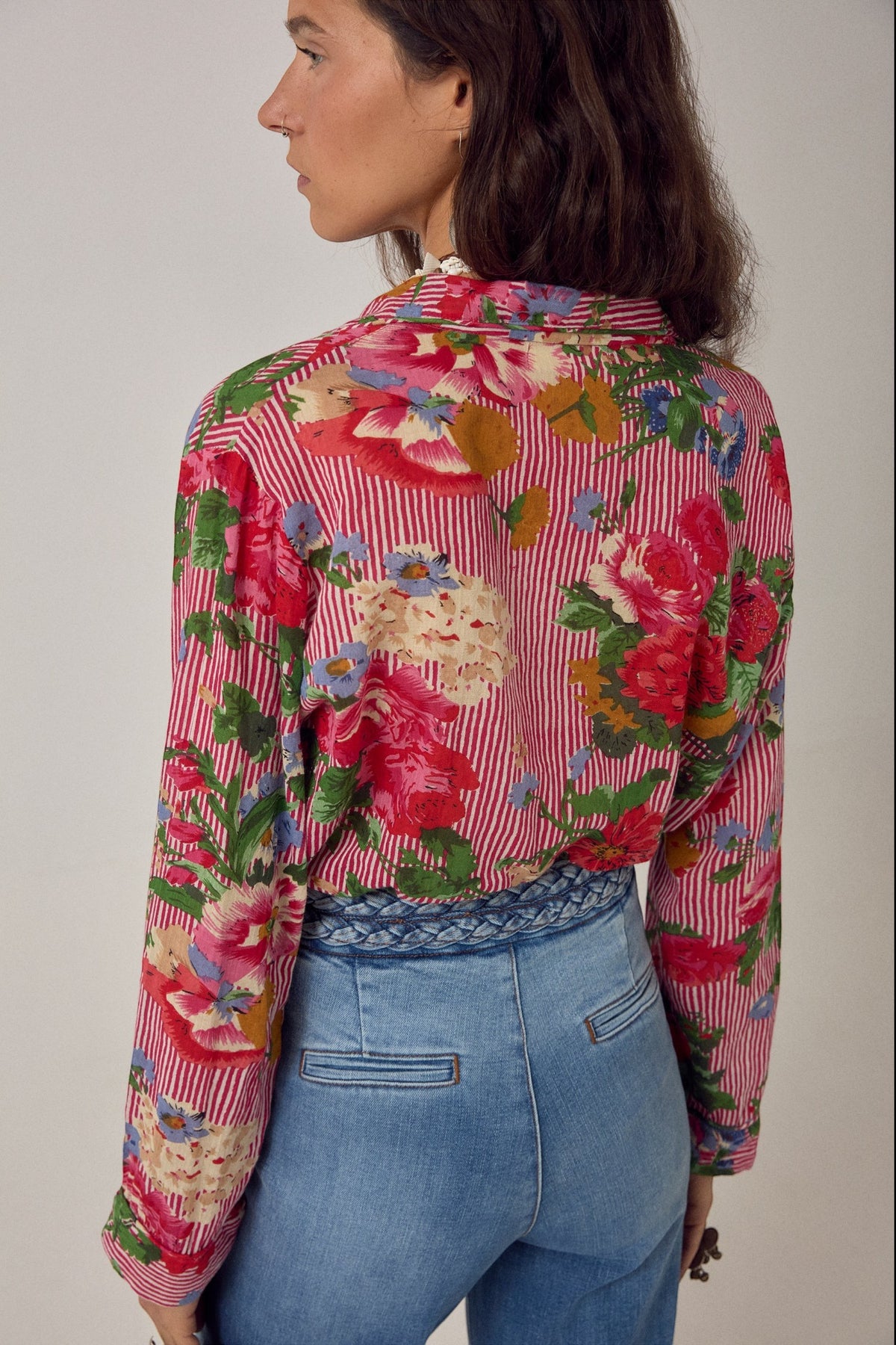 ELSHAM BOUTIQUE Piti shirt in rouge floral print over fine stripes, worn tucked into blue jeans, back view.