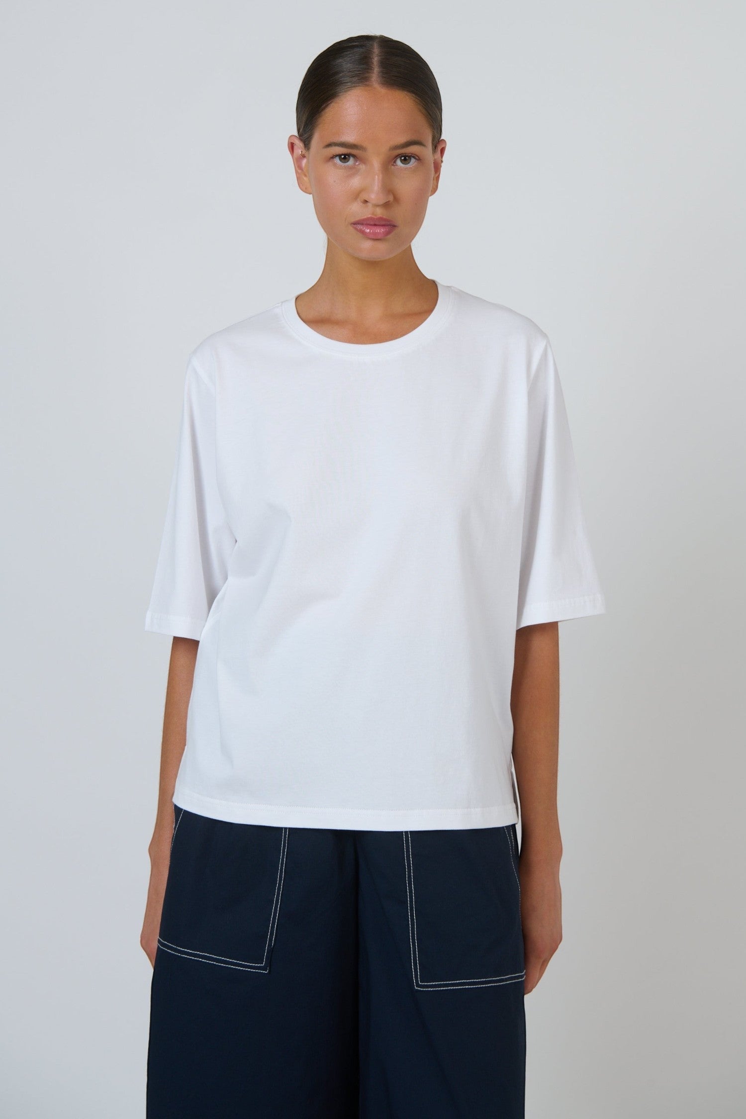 Model wearing an ELSHAM BOUTIQUE white cotton crew neck top with a relaxed boxy fit and elbow-length drop sleeves.
