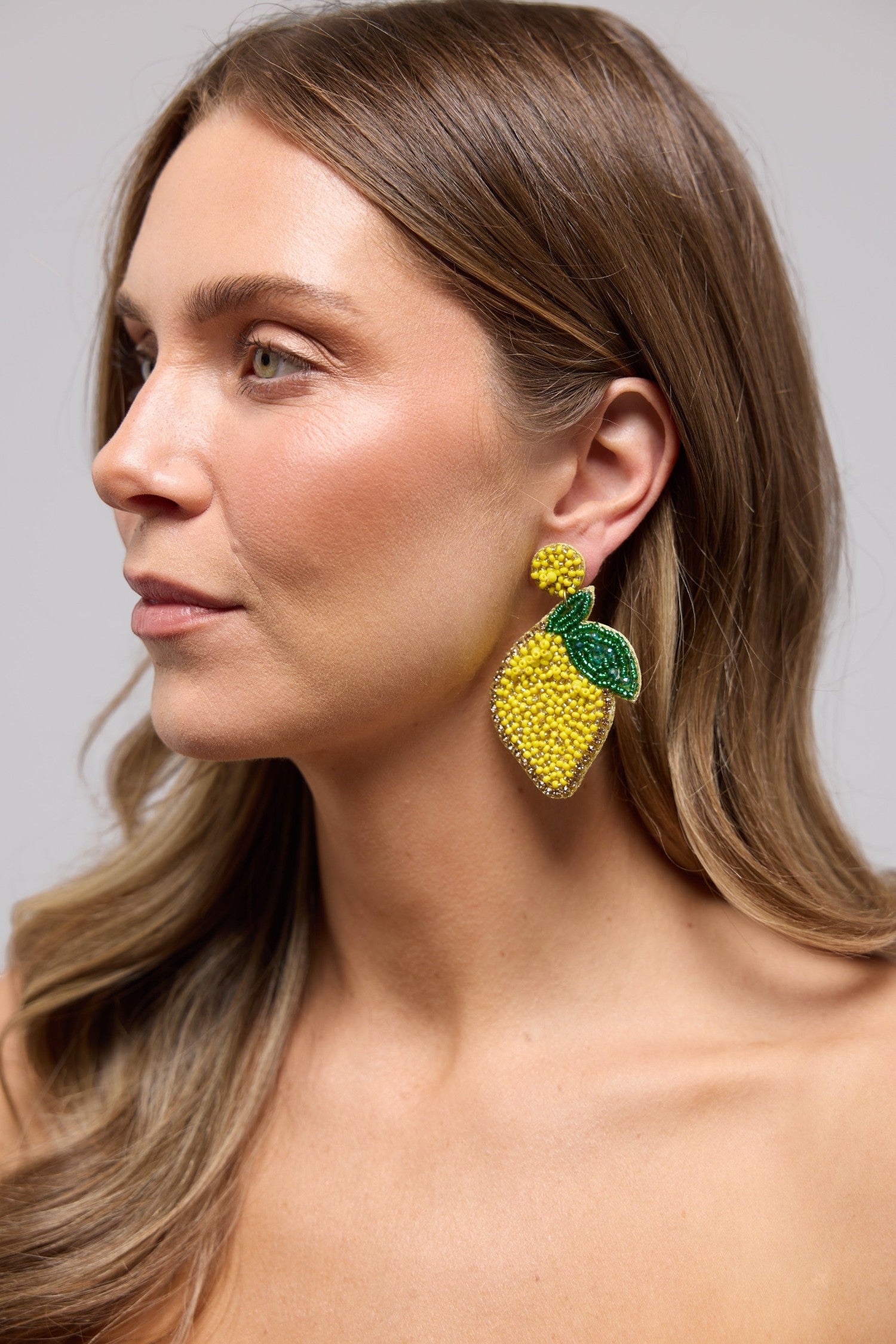 ELSHAM BOUTIQUE hand-beaded lemon statement earrings with green leaf detail worn by a woman in profile