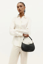 Model holding an ELSHAM BOUTIQUE black calf nappa mini sling bag with brass hardware and a detachable top handle.