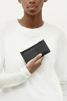 ELSHAM BOUTIQUE black grained calf leather zip card holder with brass hardware held in hand against white background