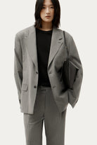 ELSHAM BOUTIQUE Mini Chopalopagus black leather crossbody bag with brass hardware worn by a model in a grey suit.