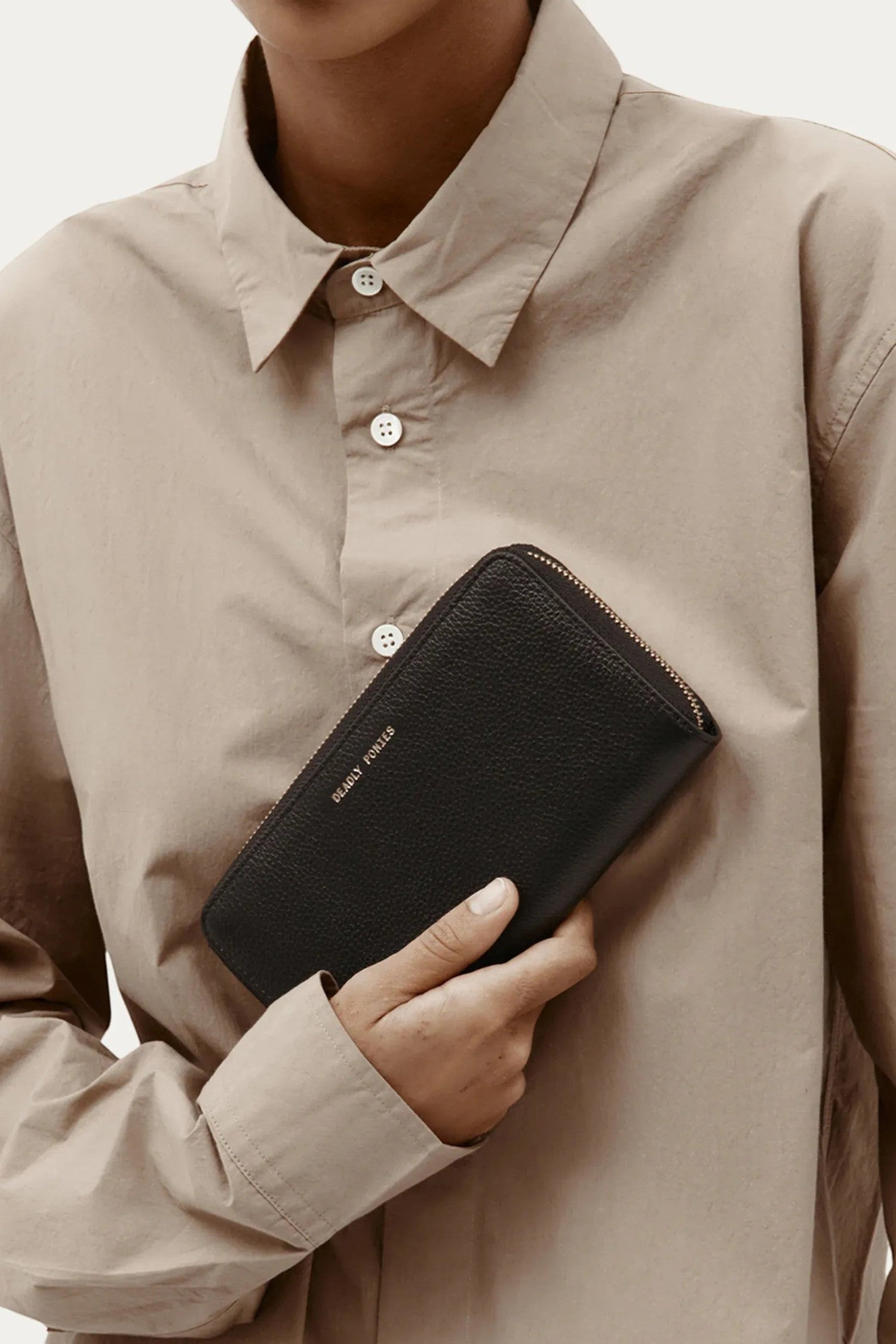 ELSHAM BOUTIQUE black grained calf leather maxi wallet with brass zip closure held by a person in a beige shirt