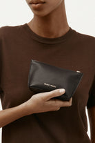 ELSHAM BOUTIQUE black calf nappa leather mini pouch with brass zip closure and gold foil logo held in hand