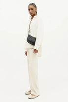 ELSHAM BOUTIQUE black calf nappa leather mini sling bag with brass hardware worn crossbody by a model in white
