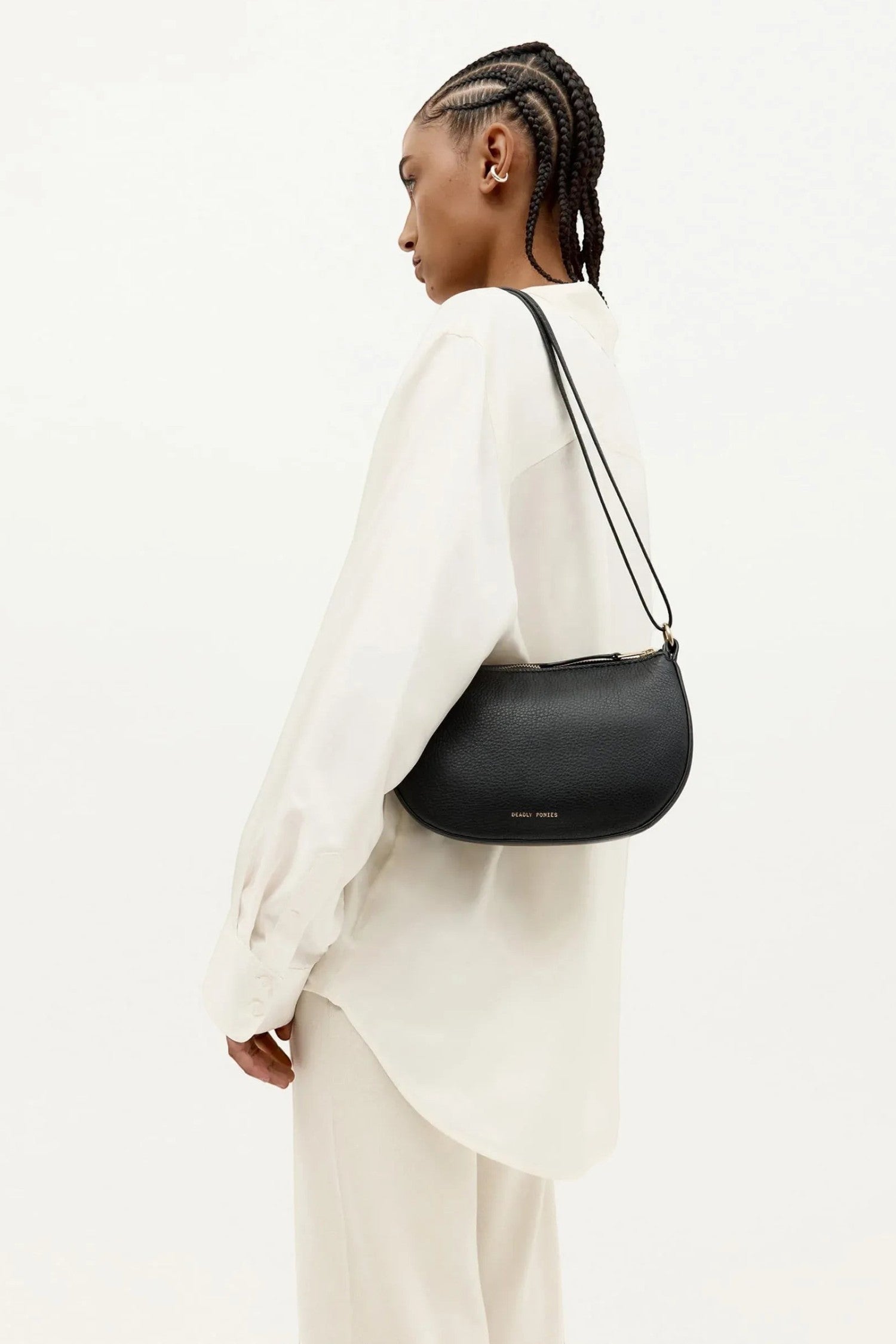 ELSHAM BOUTIQUE black calf nappa mini sling bag with brass hardware worn over the shoulder by a model in a white shirt