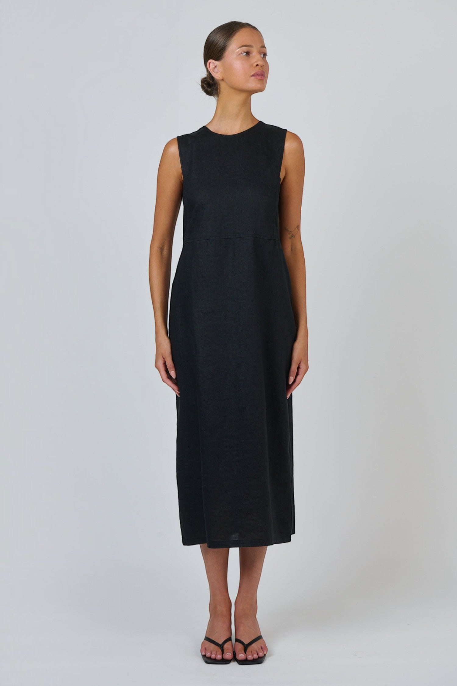 Model wearing an ELSHAM BOUTIQUE black sleeveless linen midi dress with a round neckline and fitted bodice