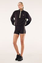 Model wearing ELSHAM BOUTIQUE black Echo quarter zip jacket with contrast binding and adjustable waist drawcords