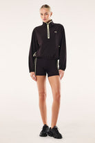 Model wearing ELSHAM BOUTIQUE black Echo quarter zip jacket with contrast binding and adjustable waist drawcords
