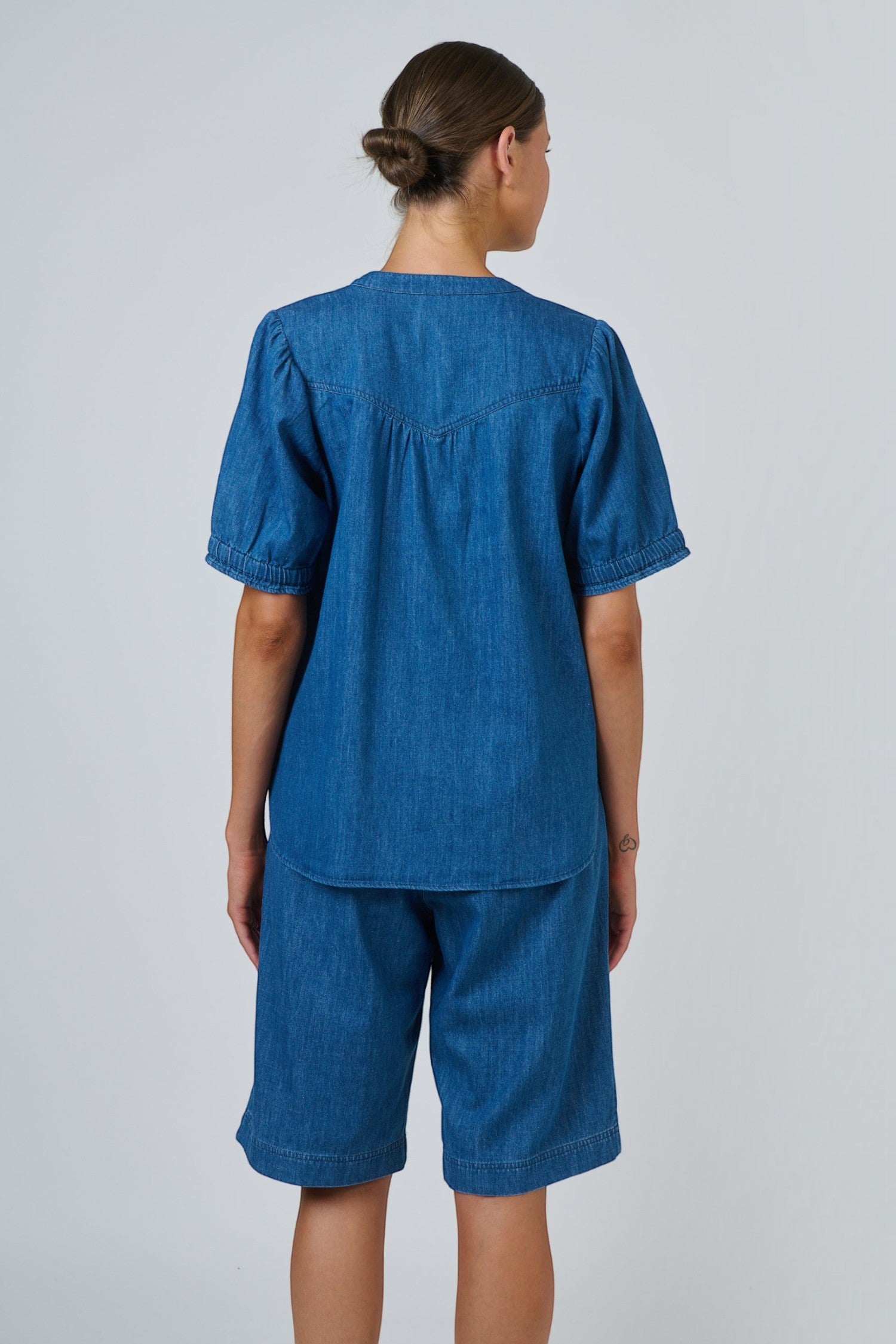 Back view of ELSHAM BOUTIQUE chambray linen blouse with puffed sleeves and gathered back yoke on a model