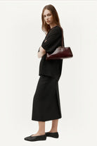 Model wearing an ELSHAM BOUTIQUE dark cherry glossy calf leather Mini Vault Tote with fixed handles and metal frame.