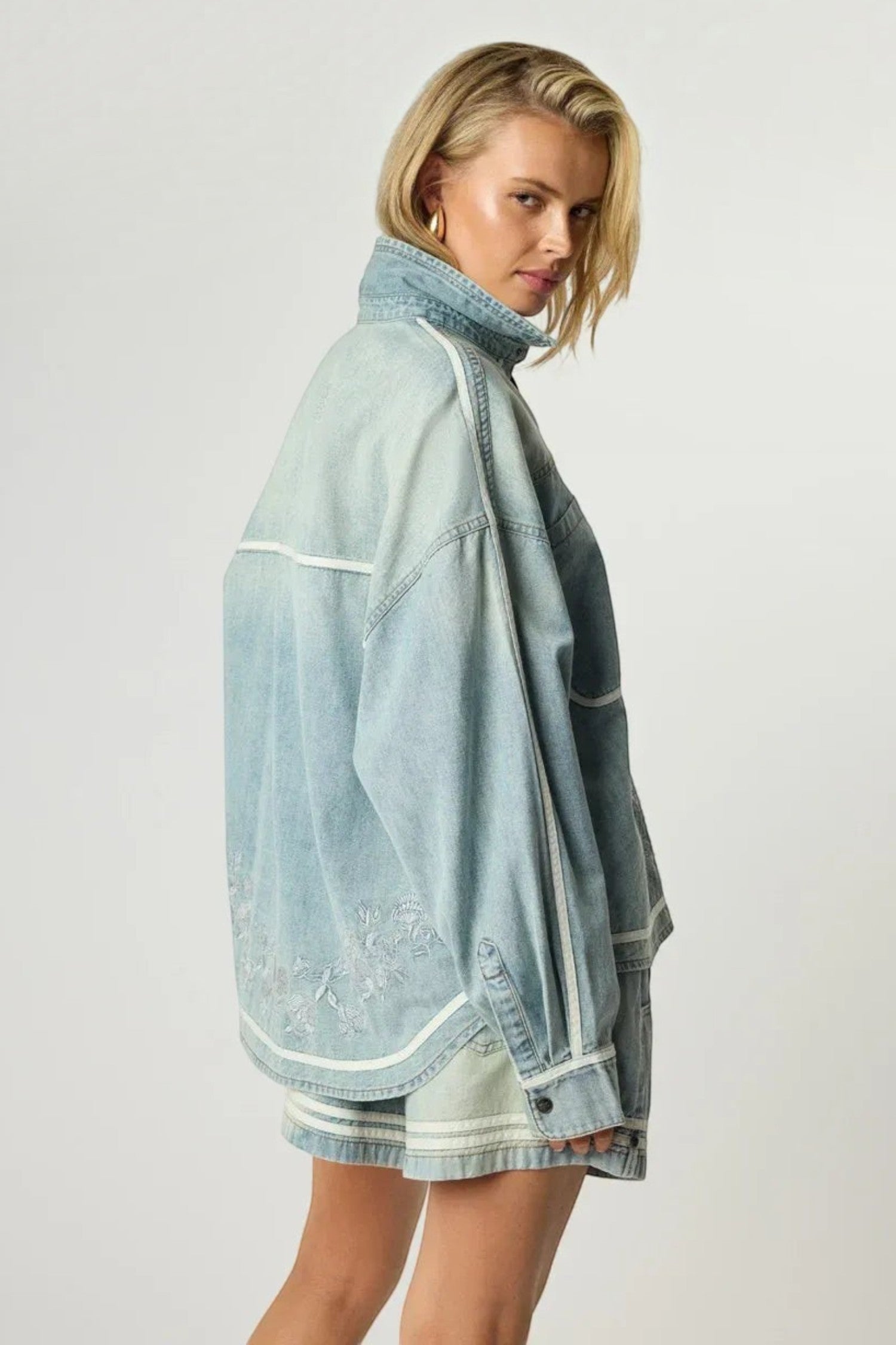 ELSHAM BOUTIQUE oversized chambray blue denim shirt with delicate embroidery and white piping, worn by a blonde model.