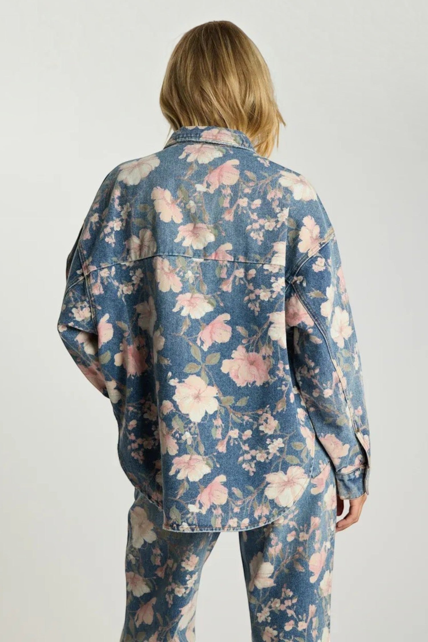 Back view of a woman wearing an ELSHAM BOUTIQUE oversized blue denim shacket with a vibrant pink floral print.