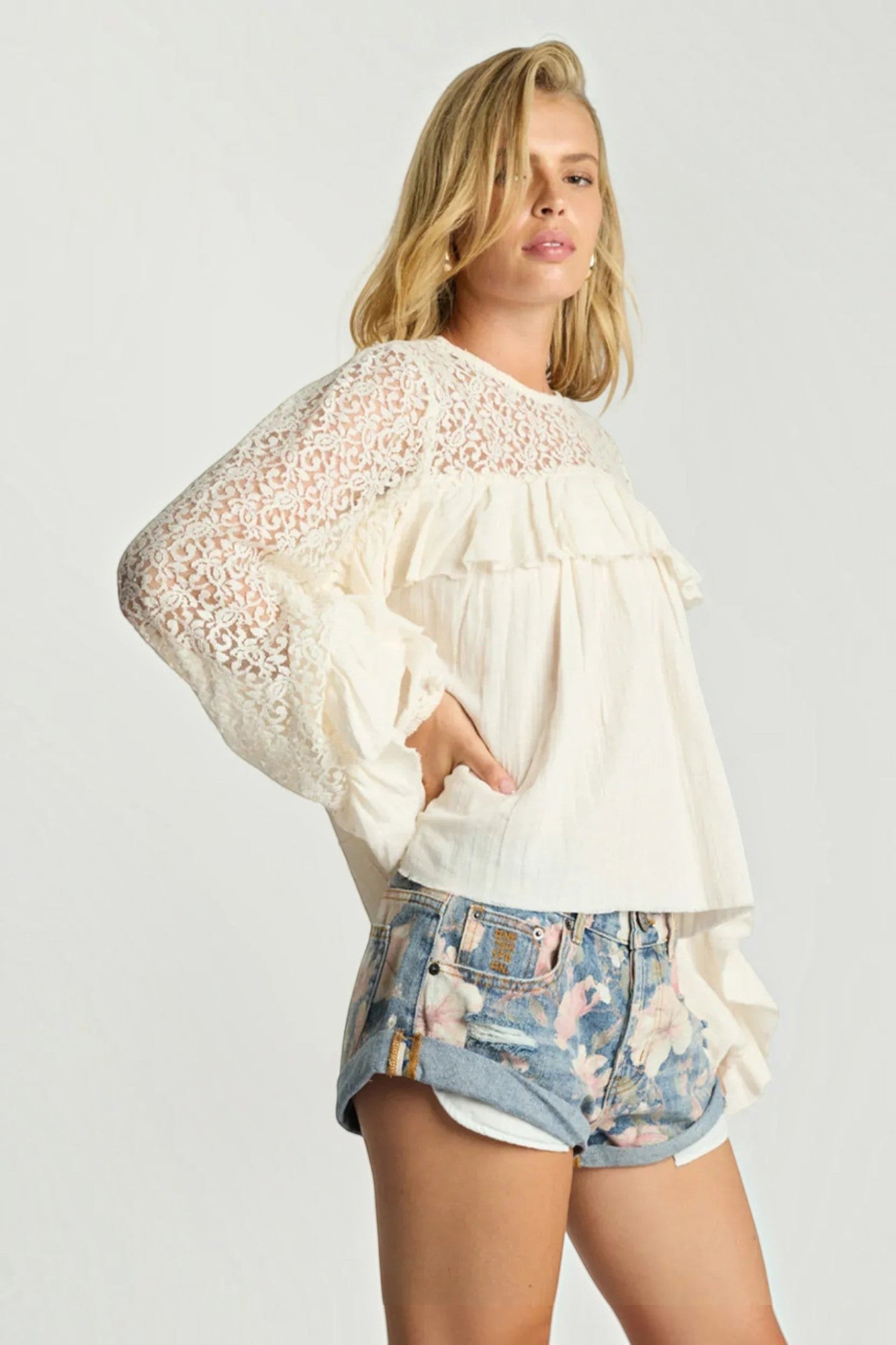 Model wearing ELSHAM BOUTIQUE ivory cotton blouse with lace sleeves, frill detailing, and a high neckline.