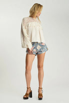 ELSHAM BOUTIQUE ivory cotton blouse with lace sleeves and frill details worn with floral denim shorts and heels