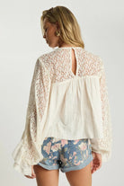 ELSHAM BOUTIQUE ivory cotton blouse with sheer lace back, long frilled sleeves, and keyhole closure worn with shorts.