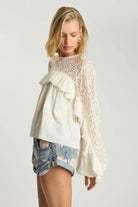 ELSHAM BOUTIQUE ivory cotton blouse with sheer lace sleeves, high neckline, and cascading frills on a blonde model.