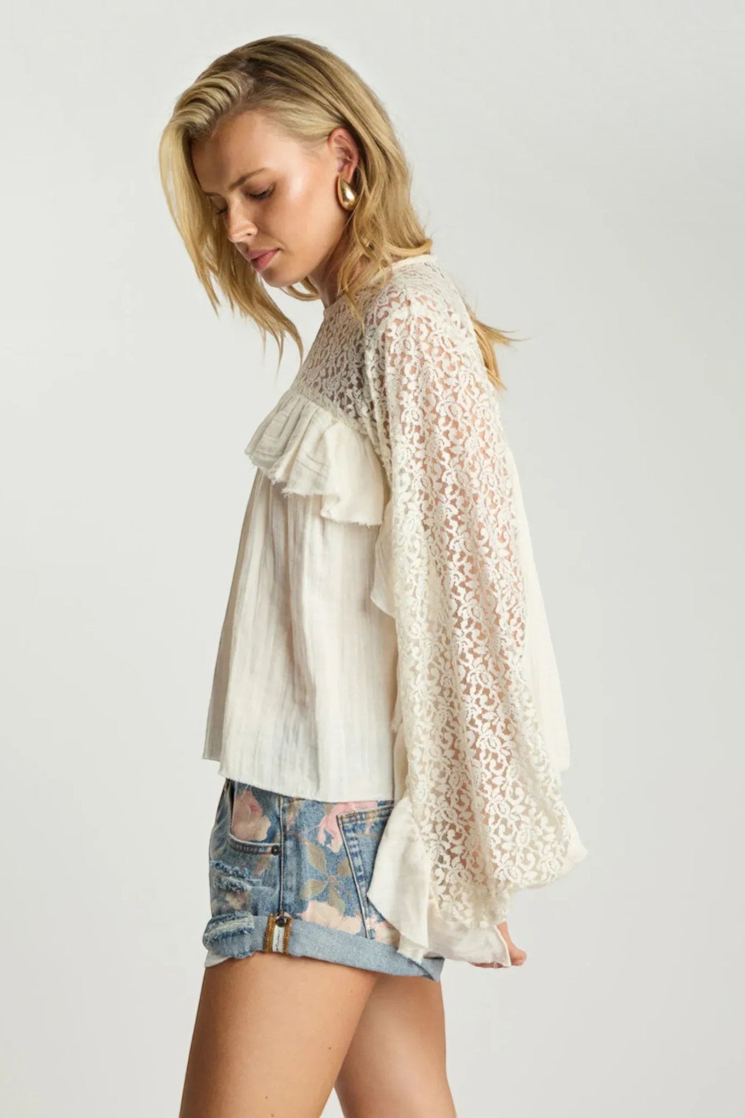 ELSHAM BOUTIQUE ivory cotton blouse with sheer lace sleeves and cascading frills worn by a model in denim shorts