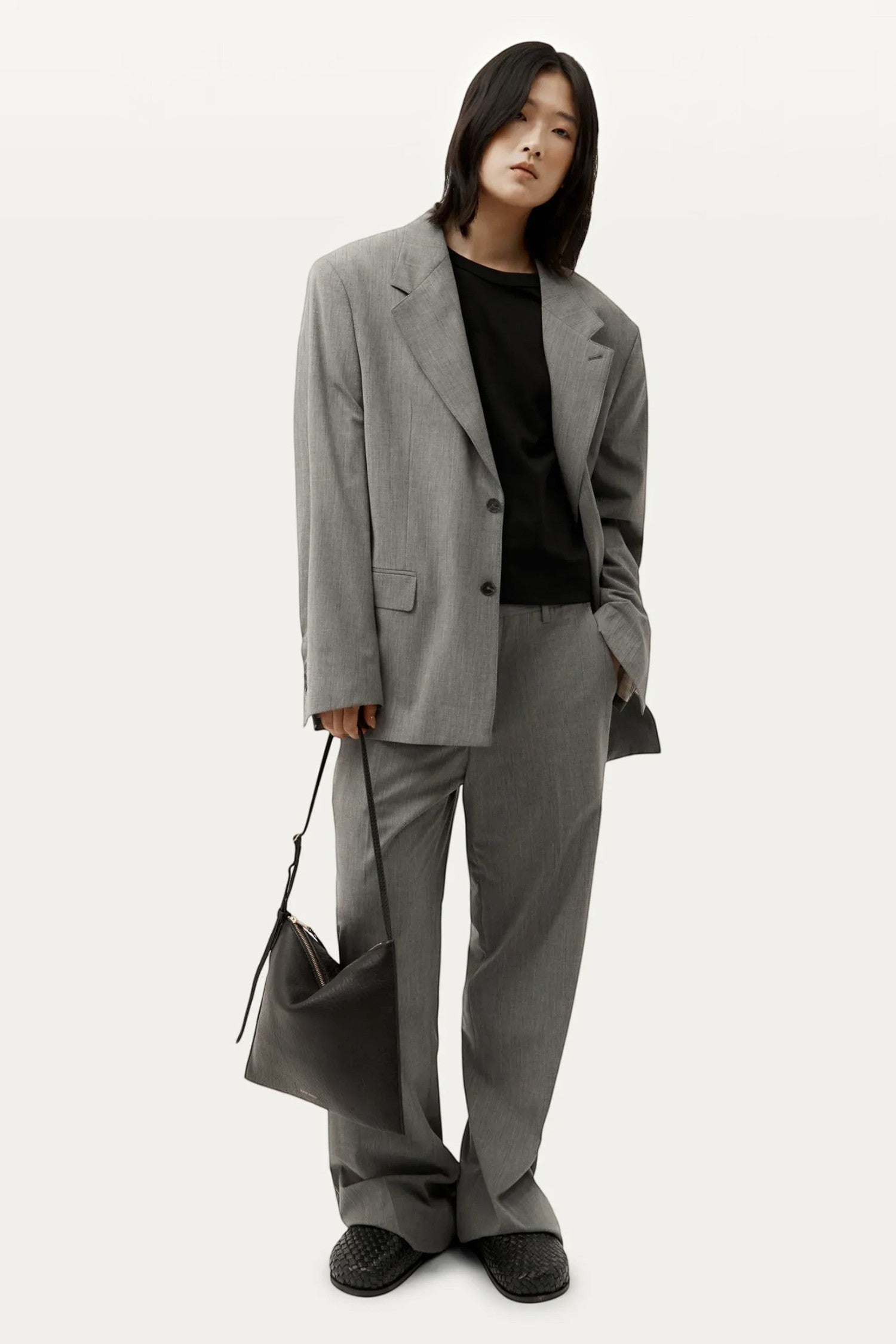 ELSHAM BOUTIQUE Mini Chopalopagus black leather bag with brass hardware held by a model in a grey suit