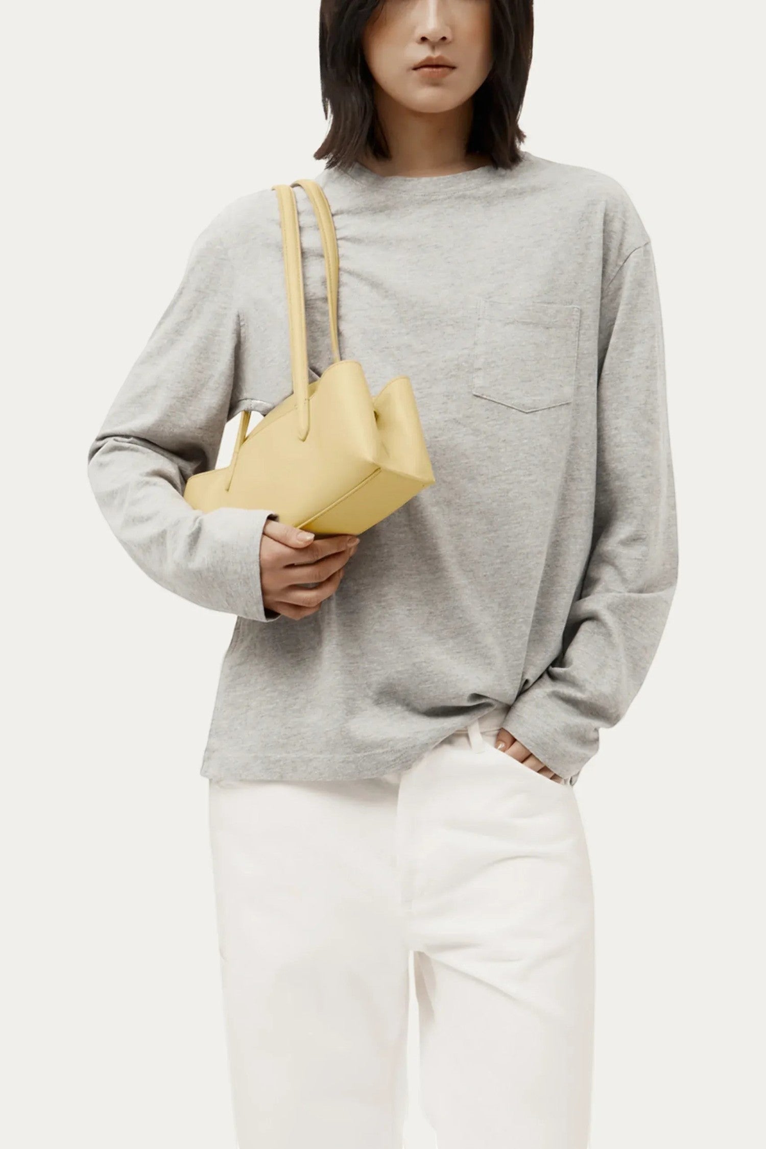Model wearing an ELSHAM BOUTIQUE Mini Vault Tote in lemonade yellow ironed calf nappa leather with dual top handles.