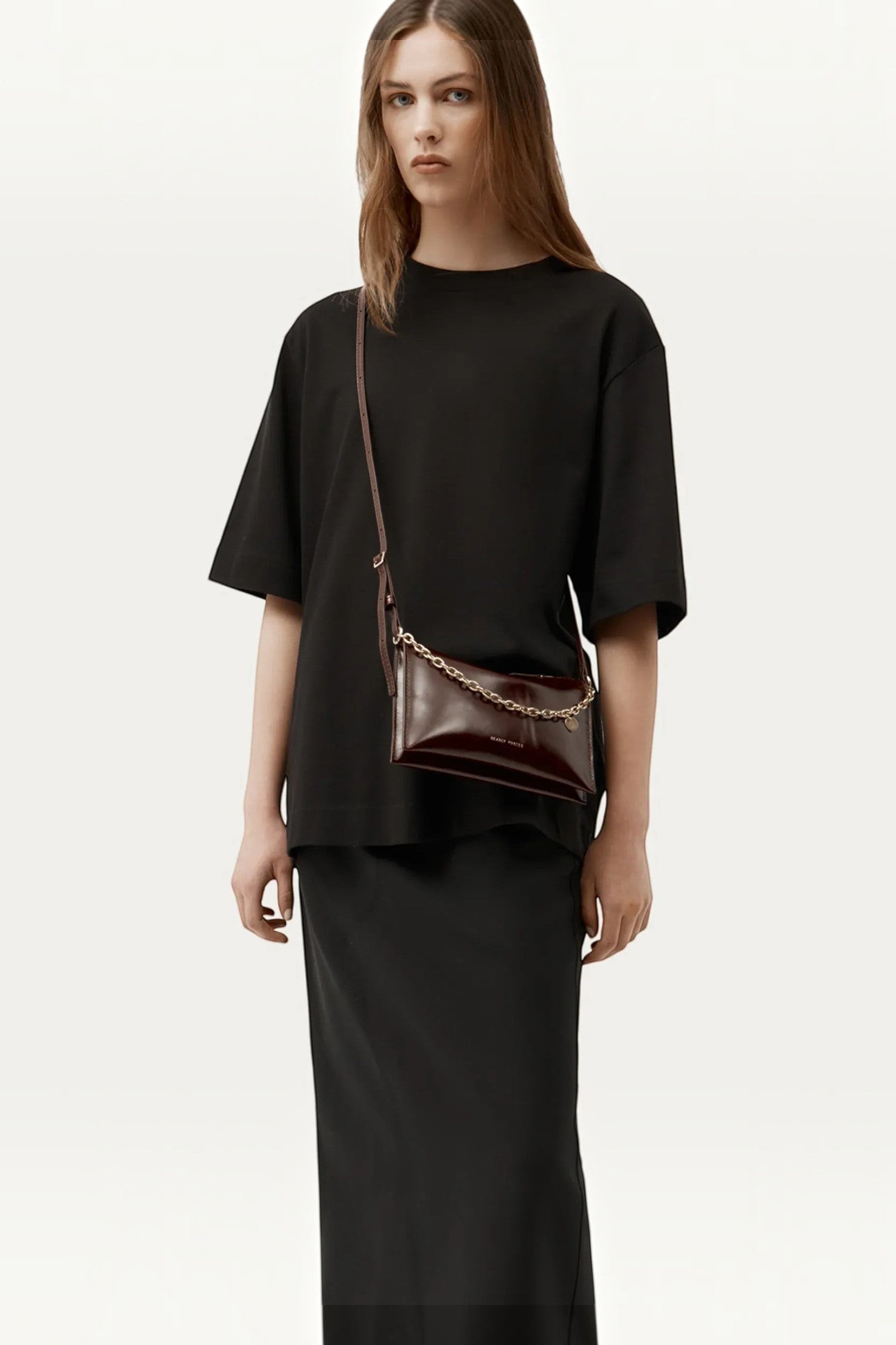 Model wearing ELSHAM BOUTIQUE Minimese crossbody bag in dark cherry glossy calf nappa with brass chain detail