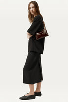 ELSHAM BOUTIQUE Minimese crossbody bag in dark cherry glossy calf nappa with gold chain, worn by a model in black.
