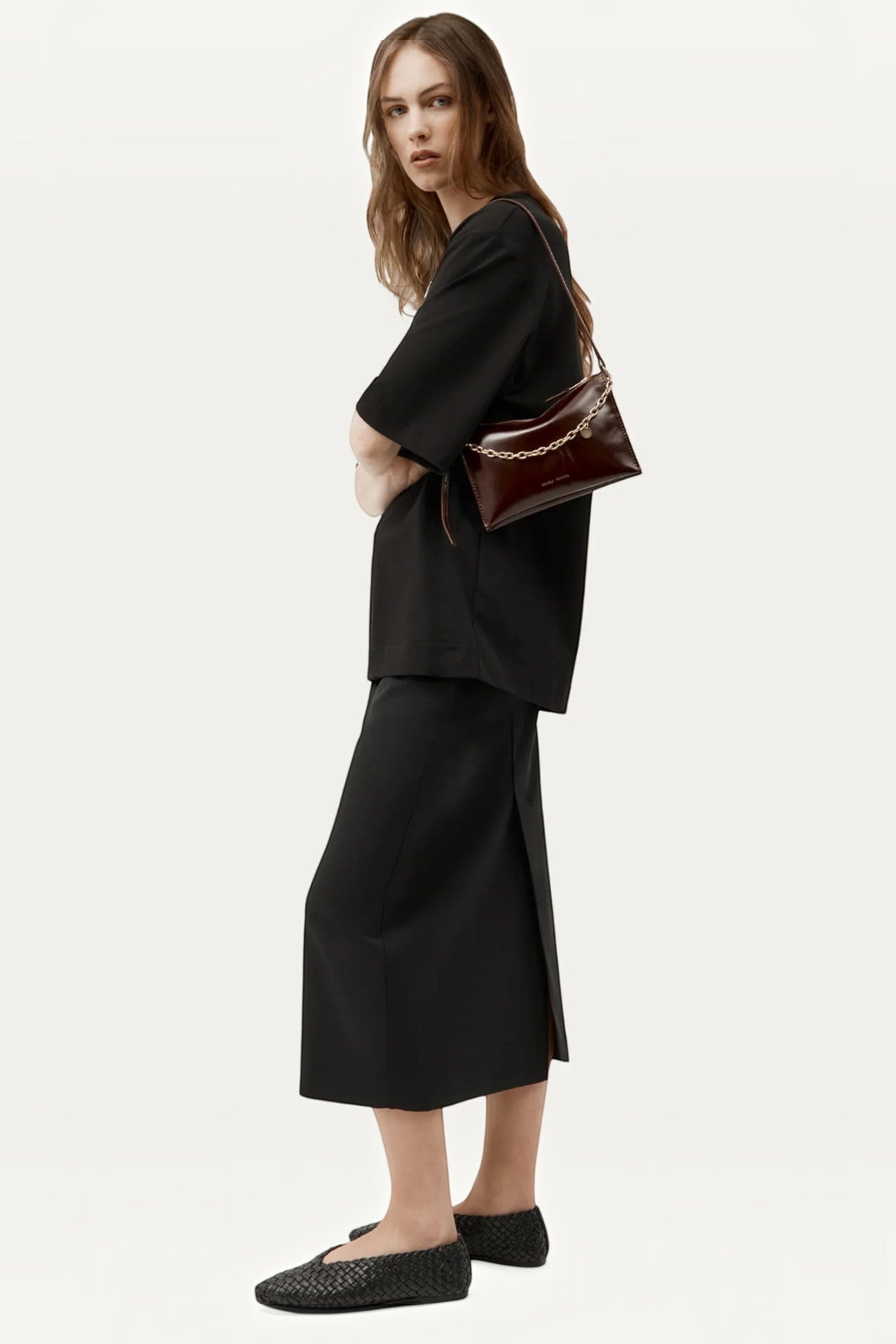ELSHAM BOUTIQUE Minimese crossbody bag in dark cherry glossy calf nappa with gold chain, worn by a model in black.
