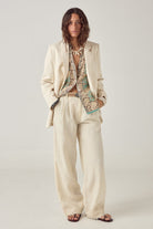 Model wearing ELSHAM BOUTIQUE Otto ivory cotton-linen straight-leg pants with subtle pleats and embroidered hem detail.