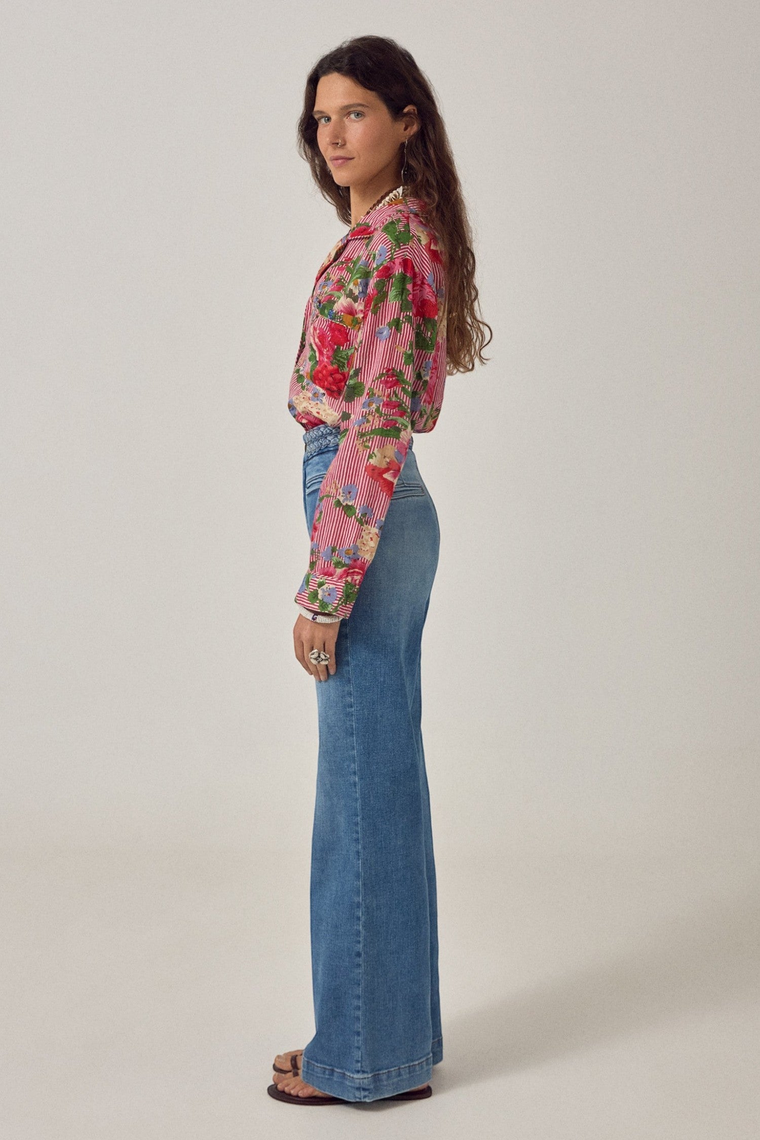 Model wearing ELSHAM BOUTIQUE Piti shirt in rouge with floral print and stripes, paired with blue flared jeans.