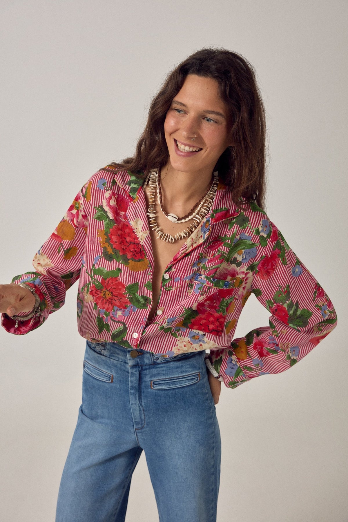 ELSHAM BOUTIQUE Piti shirt in rouge cotton with a bold floral print over fine stripes, worn by a smiling woman.