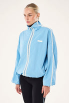 Model wearing ELSHAM BOUTIQUE Alaskan Blue Radius Jacket with funnel neck, white side stripes, and zip-up front.