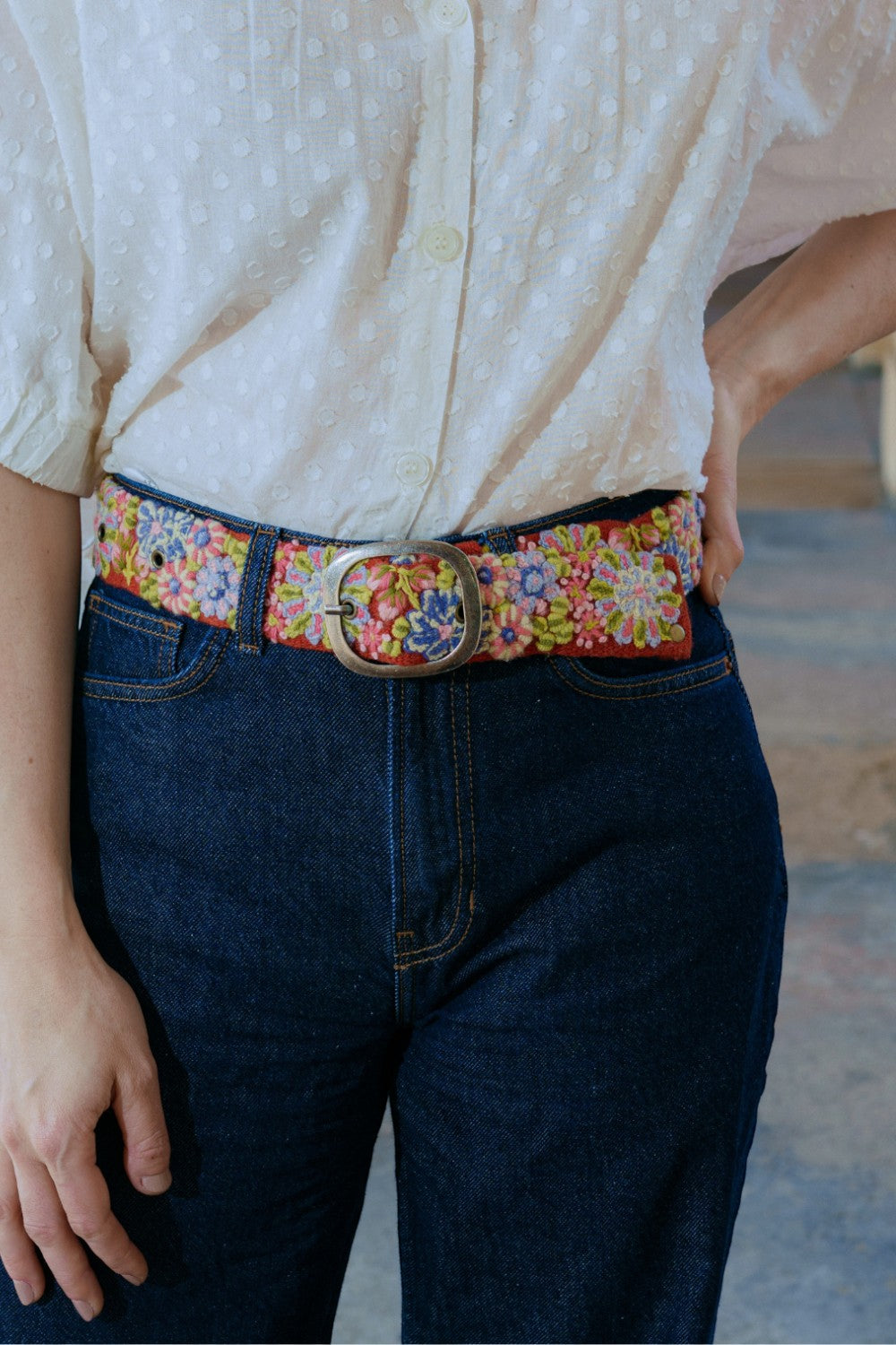 ELSHAM BOUTIQUE Teaberry wool belt with colorful floral embroidery and a metal buckle worn over dark blue jeans.