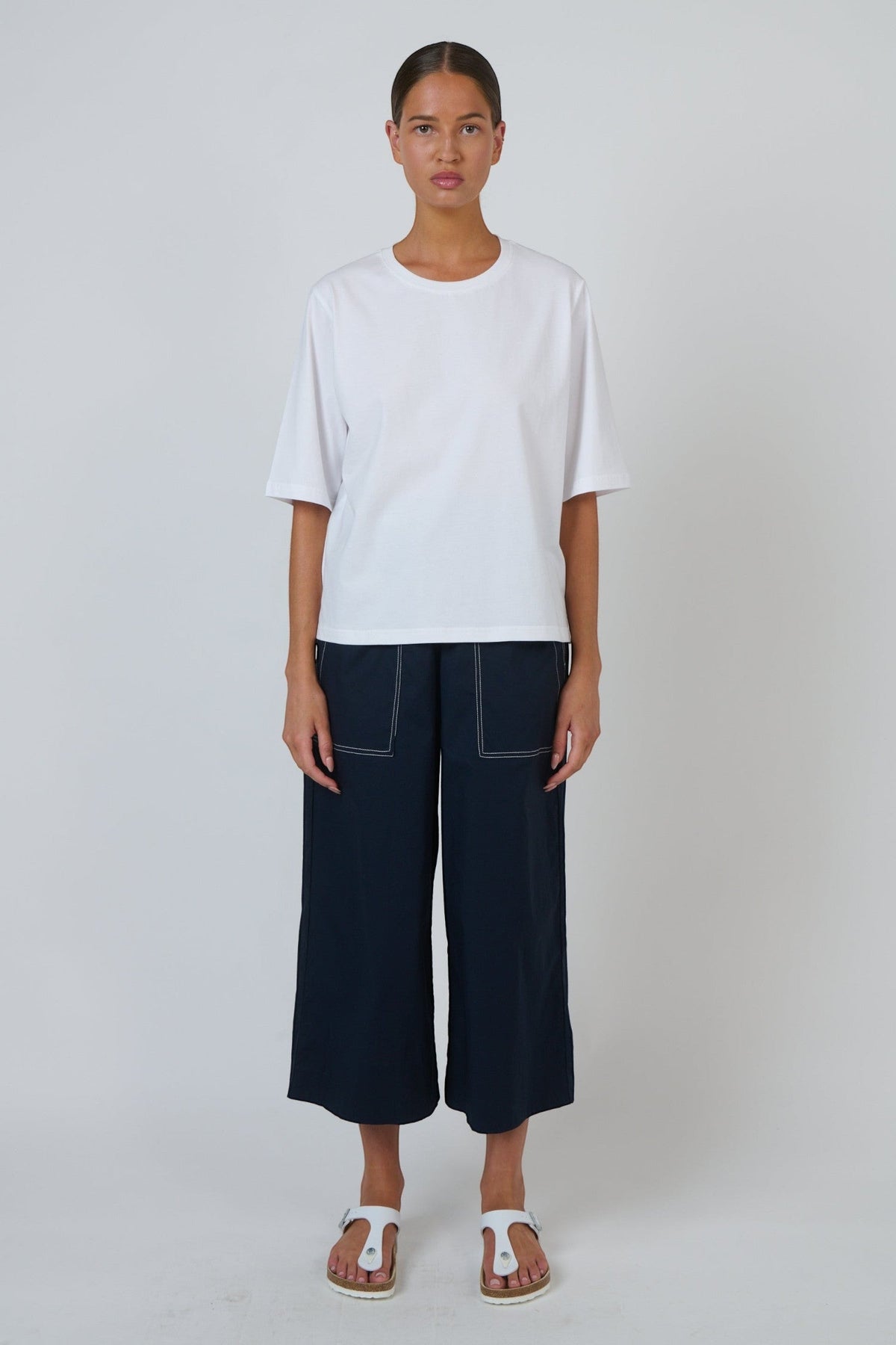 ELSHAM BOUTIQUE white cotton crew neck top with drop shoulders and boxy fit worn by a model with navy trousers