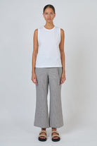 ELSHAM BOUTIQUE white cotton sleeveless top with a round neckline worn by a model with grey trousers and sandals.