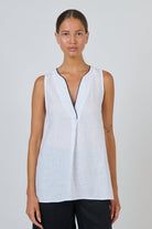 ELSHAM BOUTIQUE white sleeveless linen top with deep V-neckline and black contrast piping in an A-line silhouette.