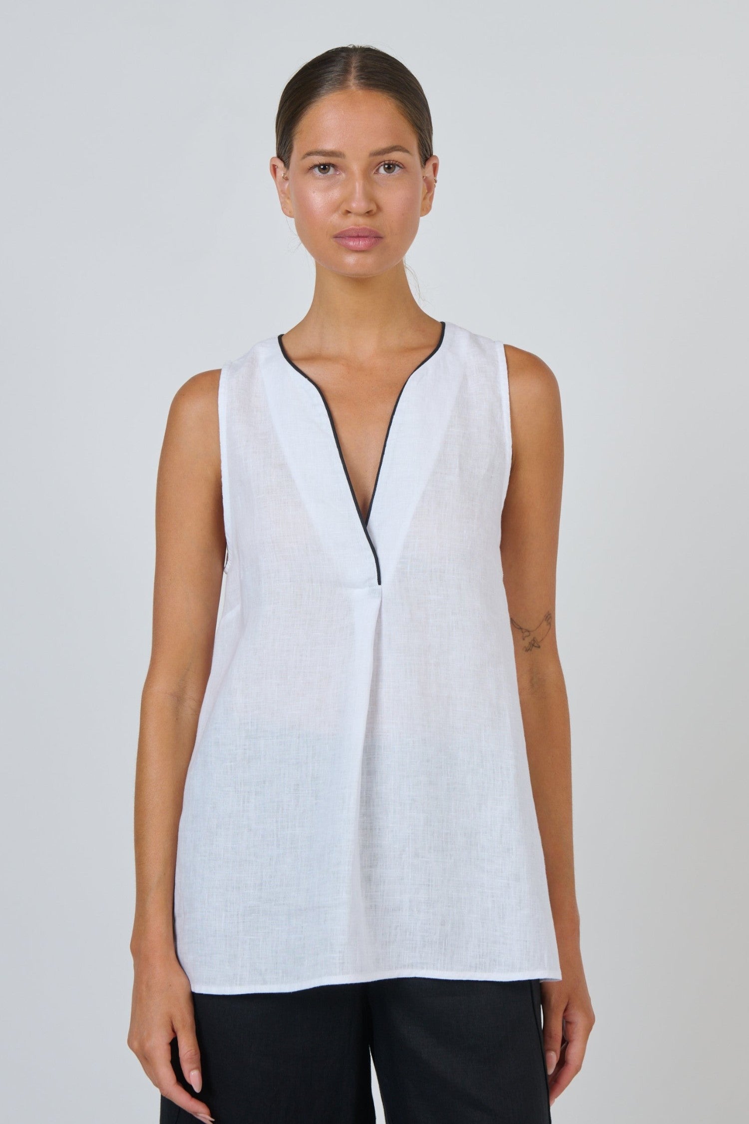 ELSHAM BOUTIQUE white sleeveless linen top with deep V-neckline and black contrast piping in an A-line silhouette.
