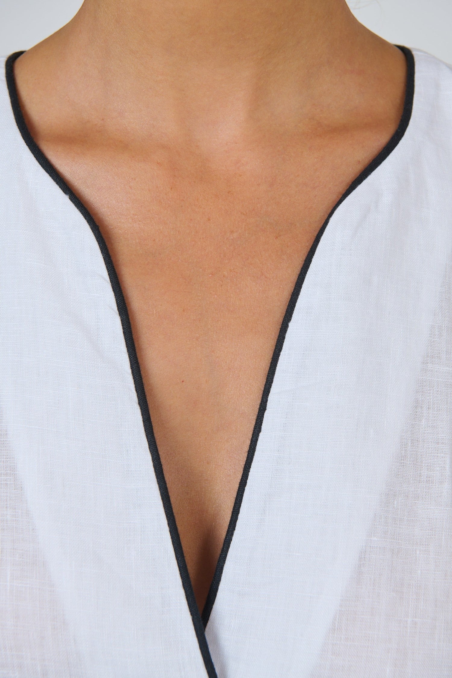 ELSHAM BOUTIQUE white linen sleeveless top featuring a deep V-neckline with elegant black contrast piping trim.