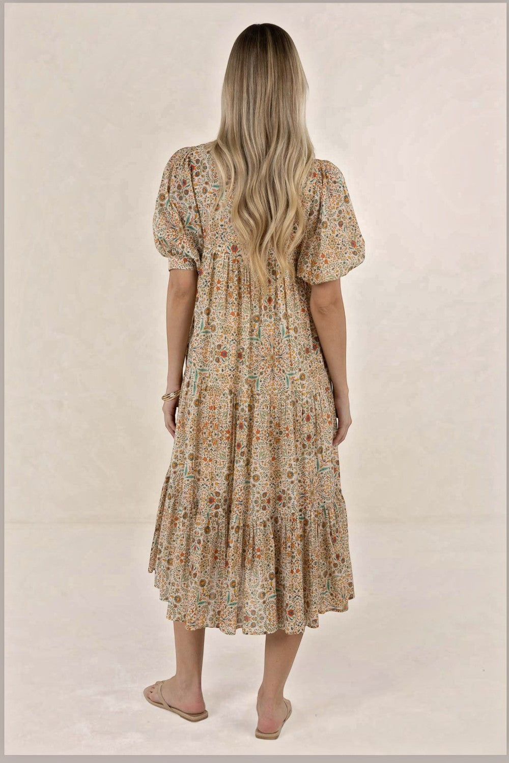 Back view of a woman wearing an ELSHAM BOUTIQUE Yasmin midi dress in almond floral print with tiered frill detailing.